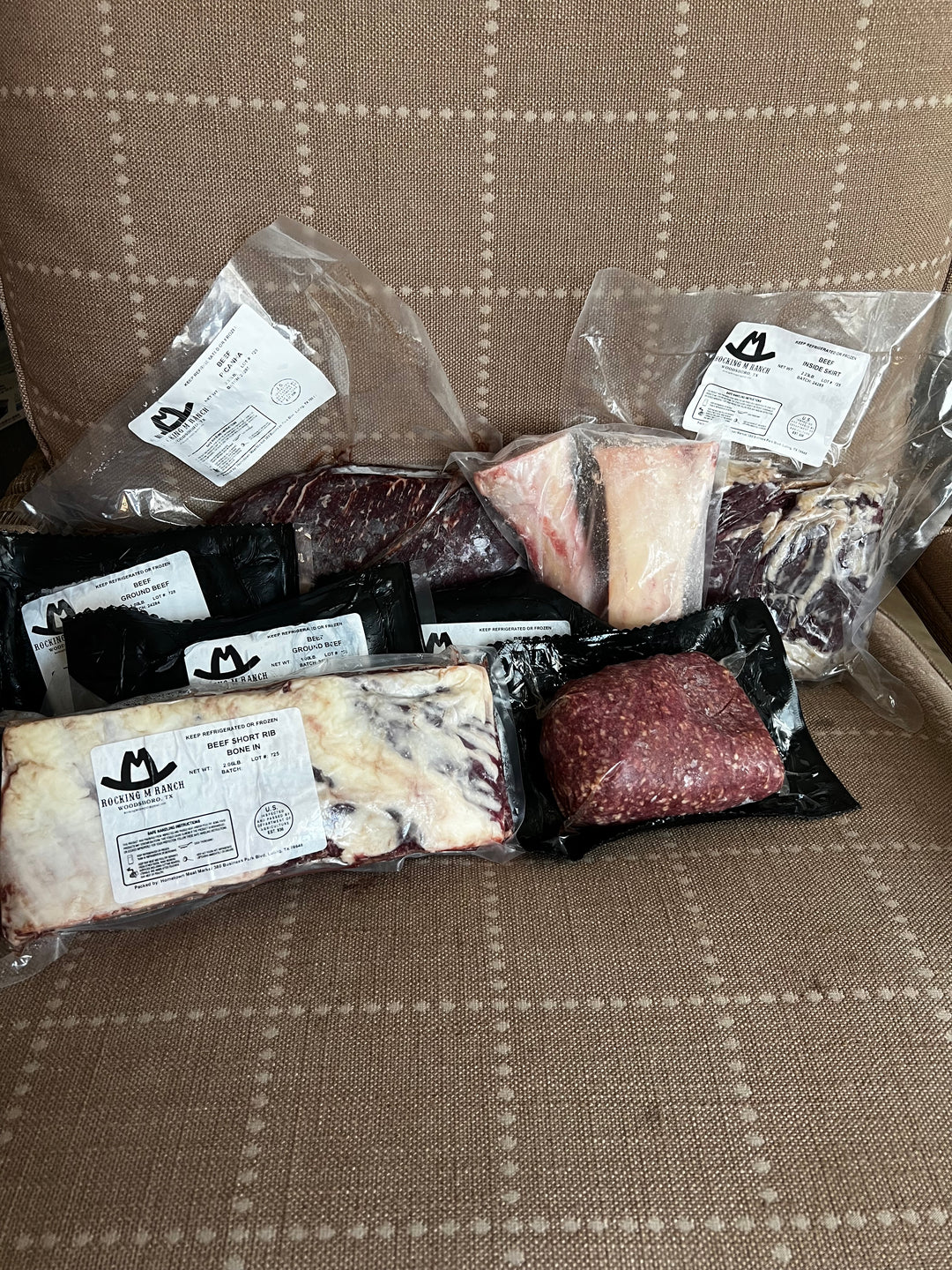 Assorted packaged meats including ground beef and various cuts, labeled with weights and origins, arranged on a table.