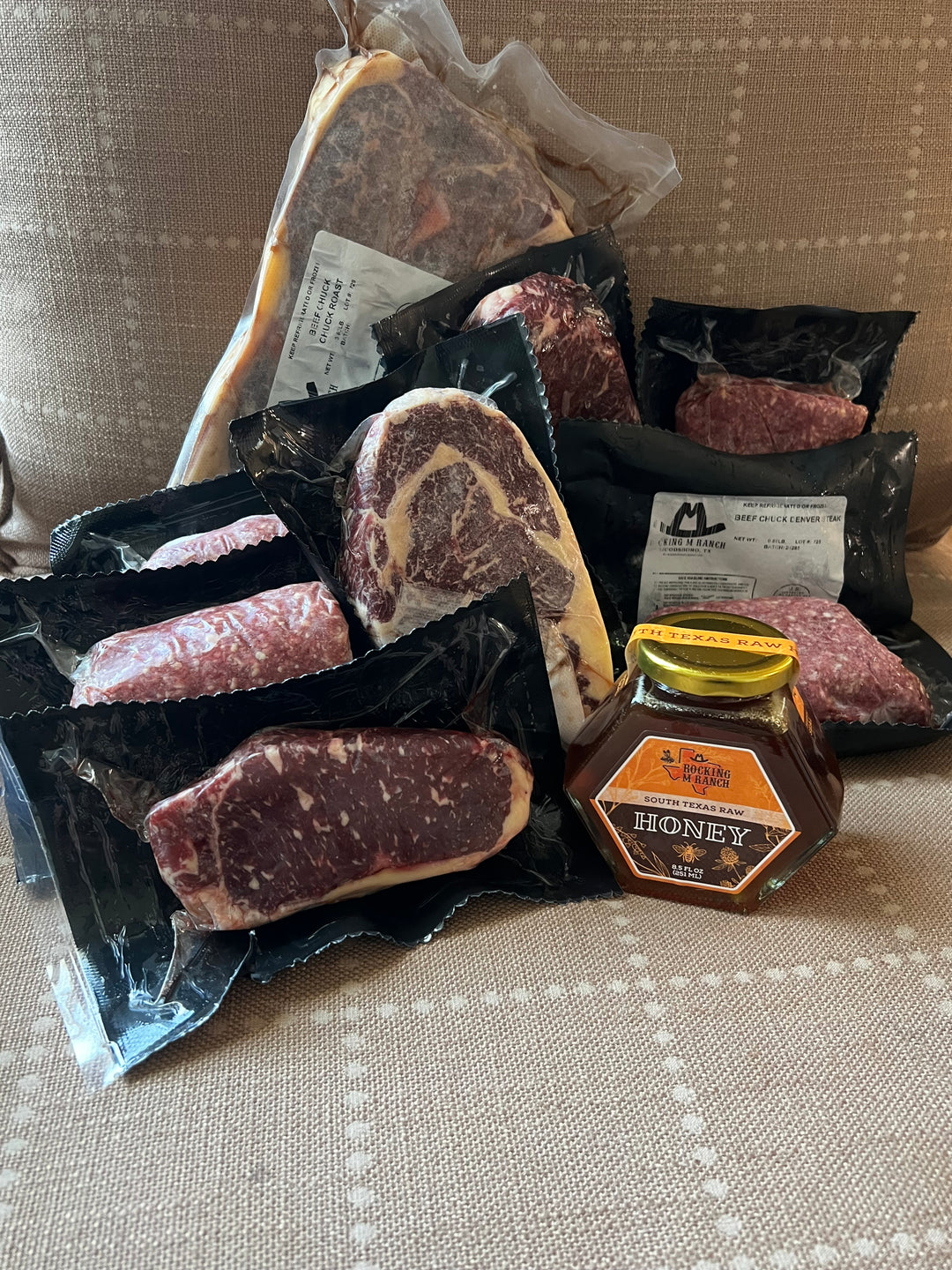Assorted packaged meats including ground beef, steaks, and a roast, accompanied by a jar of honey, all labeled with the Rocking M Ranch brand.